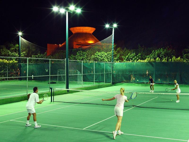 Quattro persone giocano di notte su un campo da tennis all'aperto illuminato.