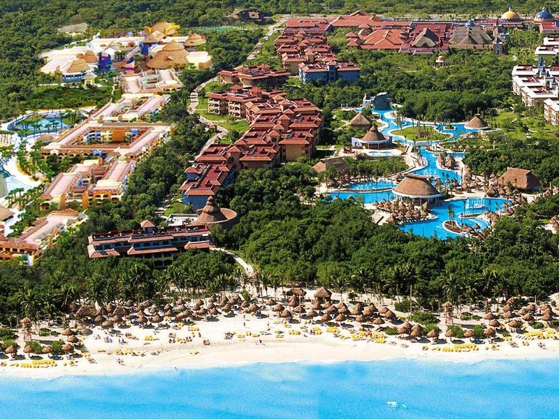 Grande resort sulla spiaggia con piscine, circondato da vegetazione rigogliosa e mare turchese.