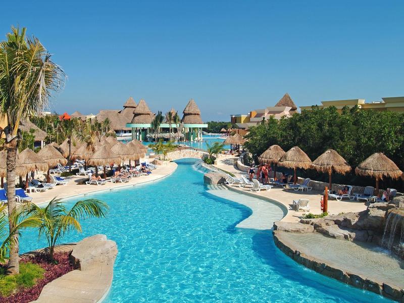 Grande piscina all'aperto con lettini e ombrelloni di paglia in un resort soleggiato.