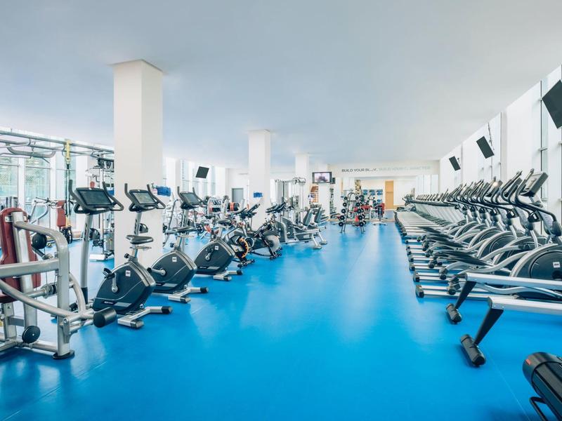 Grande palestra con file di cyclette e tapis roulant su pavimento blu.