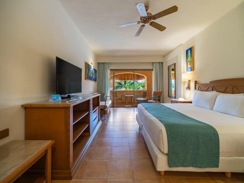 Camera d'hotel luminosa con letto grande, TV a schermo piatto e accesso al balcone con vista sul giardino.