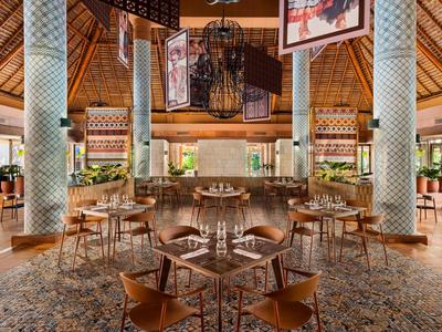 Ristorante moderno con sedie e tavoli in legno, colonne decorative e illuminazione calda.