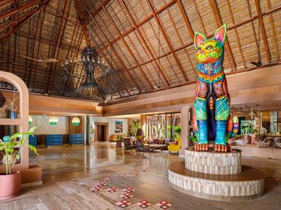 Grande scultura di gatto colorata in un ampio atrio d'hotel con tetto in legno e piante.