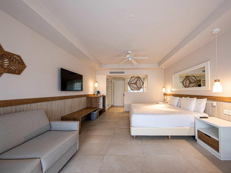 Camera d'hotel moderna con grande letto, divano e TV a parete.