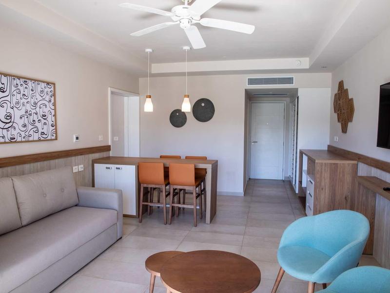 Area soggiorno moderna con divano, tavolo da pranzo, sedie blu e ventilatore a soffitto.