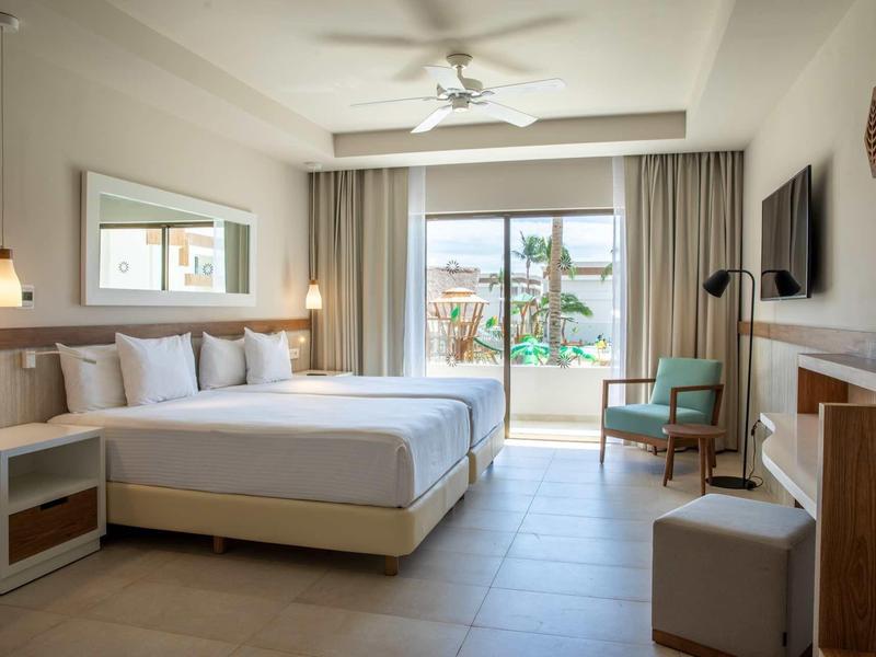 Camera d'albergo luminosa con letto grande, balcone e vista sulla piscina.