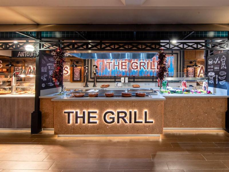Un'area buffet griglia moderna con insegna luminosa 'THE GRILL' e vari piatti.