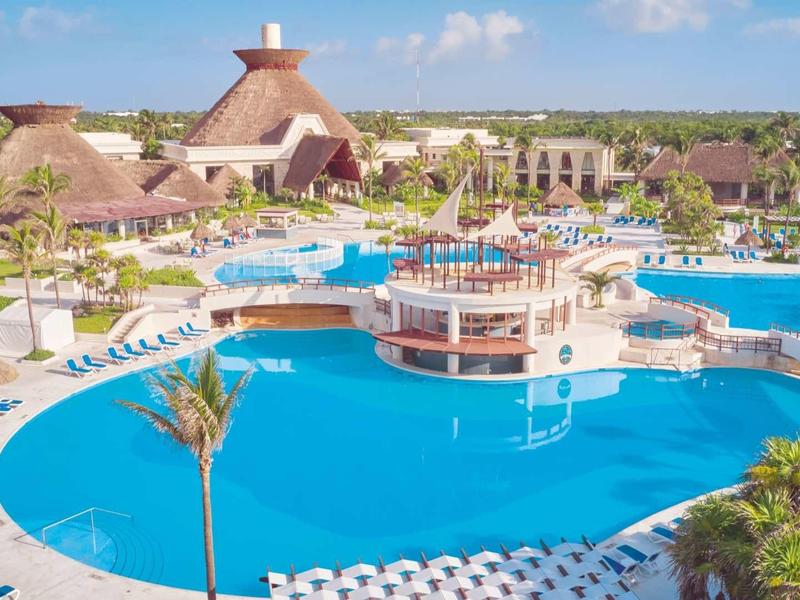Grande piscina dell'hotel con palme e numerose sdraio sotto un cielo azzurro.