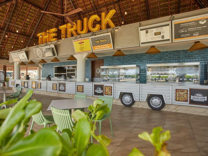 Ristorante food truck moderno con sedie e piante in ambiente tropicale.
