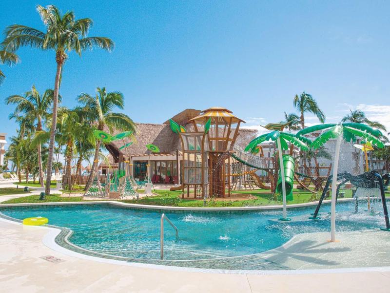 Piscina ricreativa con giochi d'acqua e palme in un contesto alberghiero tropicale.