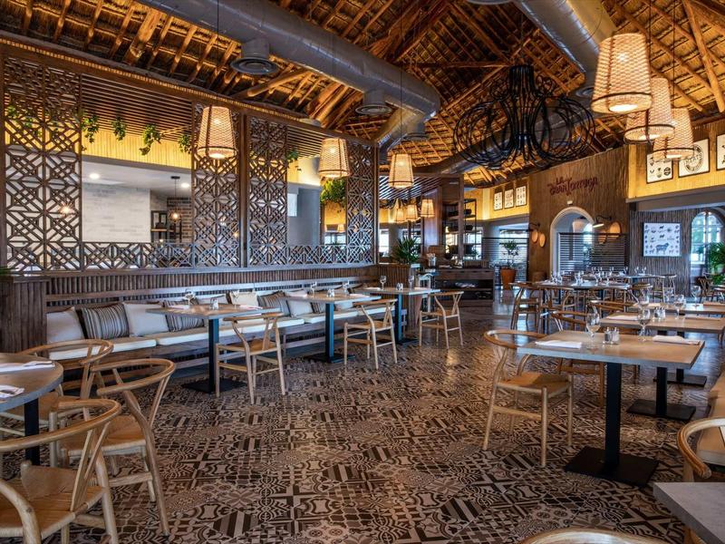 Ristorante moderno con pavimenti in legno, tavoli e sedie, illuminazione calda e piante.