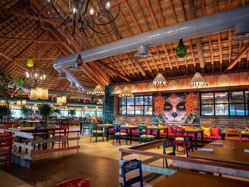 Ampia area ristorante colorata con soffitto in legno e murales vivaci.