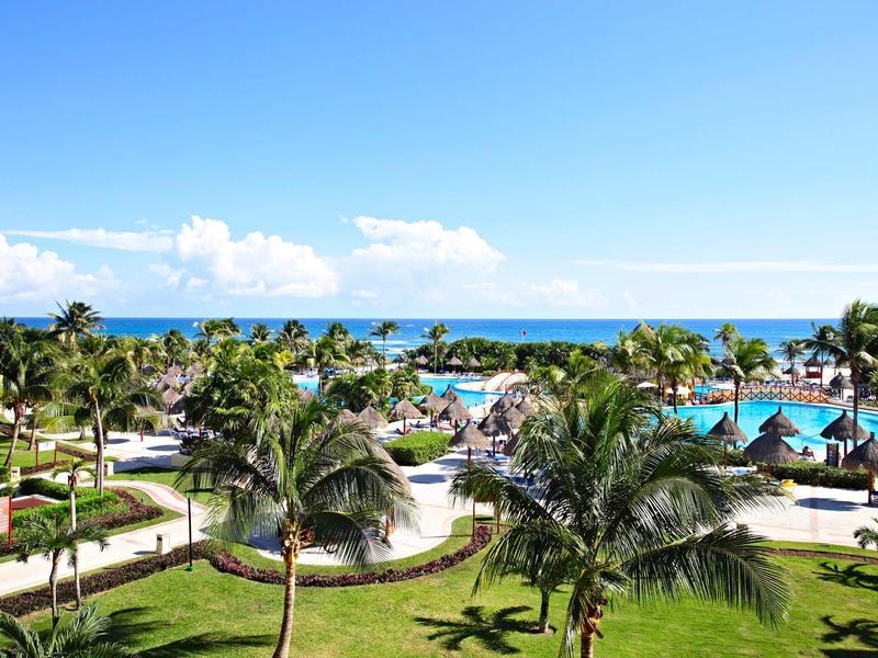 Area dell'hotel con palme, piscina e vista sull'oceano sotto un cielo sereno.