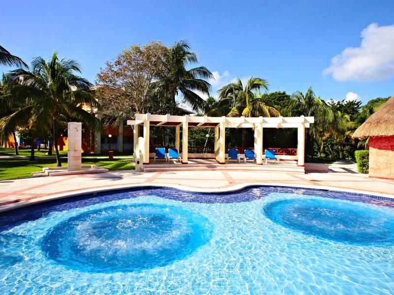 Area piscina con fontane e lettini sotto pergolati in ambiente tropicale.