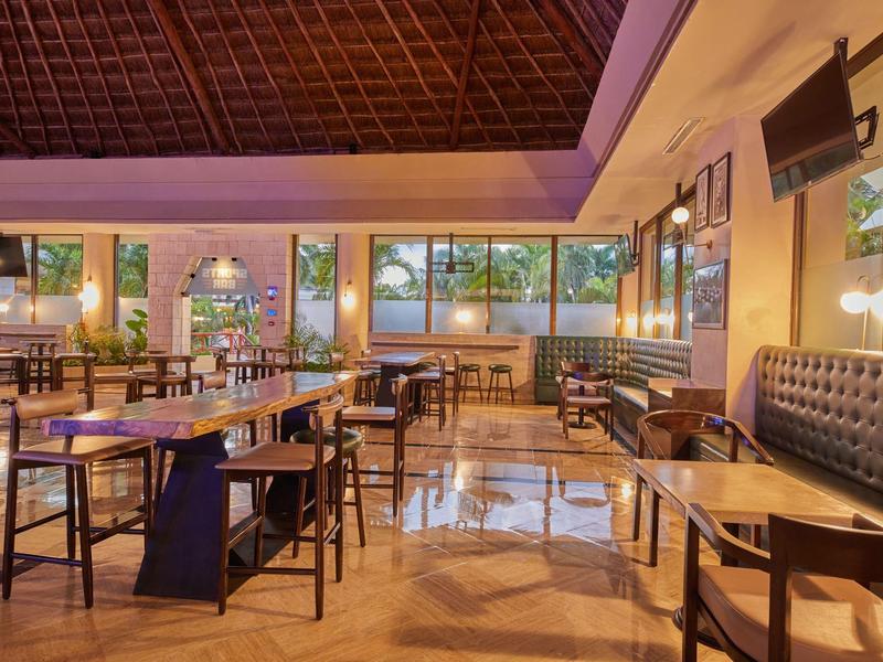 Area pranzo moderna con tavoli in legno, sedie e panca imbottita in ambiente luminoso.