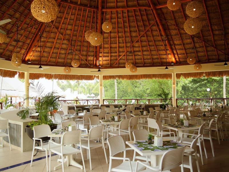 Ampia area esterna coperta di ristorante con molti tavoli e sedie circondata dalla natura.