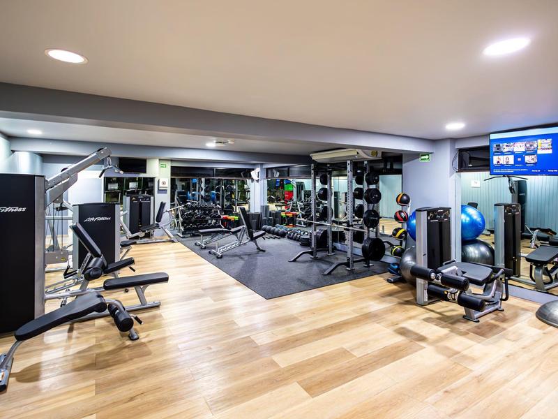 Palestra moderna con pavimento in legno, parete a specchio e vari attrezzi da allenamento.