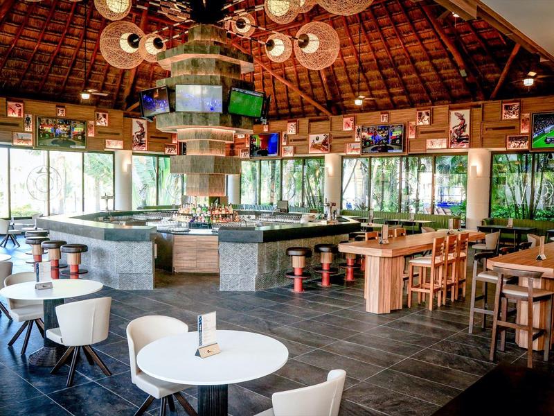 Ristorante moderno e luminoso con soffitti alti, tavoli rotondi e sedie in legno.