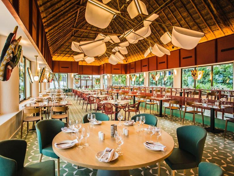 Ristorante luminoso con tetto in legno, grandi finestre, arredo moderno e tavoli apparecchiati.