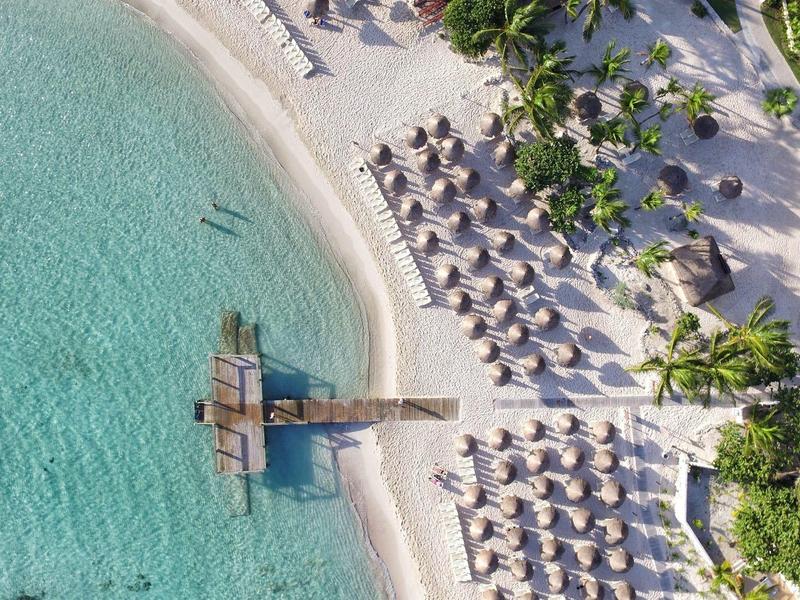 Veduta aerea di una località balneare con acqua limpida, spiaggia sabbiosa e lettini sotto ombrelloni