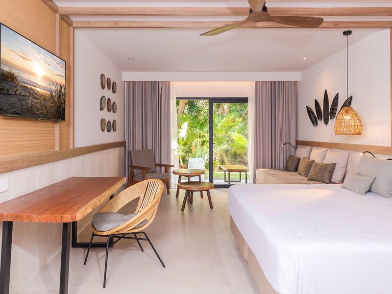 Camera d'hotel moderna con letto grande, sedie e vista su un giardino verde.