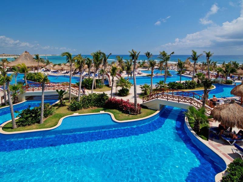 Grande piscina dell'hotel con palme e lettini sotto il cielo blu vicino al mare.