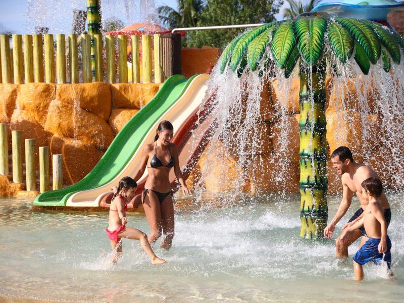 Famiglia che gioca nella piscina all'aperto con giochi d'acqua e scivolo.