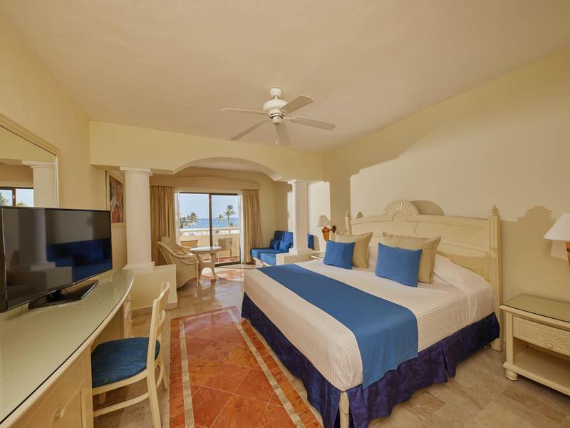 Camera d'hotel luminosa con letto grande, scrivania, TV e vista terrazza sul mare.