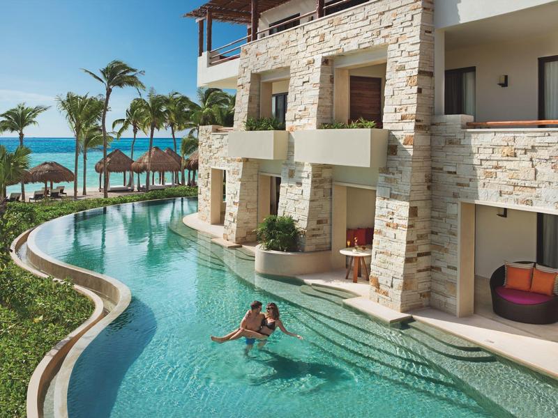 Resort con piscina a sfioro accanto a un edificio con vista sul mare e palme.