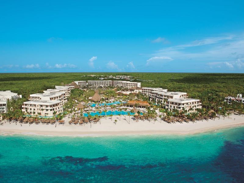Resort di lusso sulla spiaggia con più edifici, piscine e palme sul mare turchese.