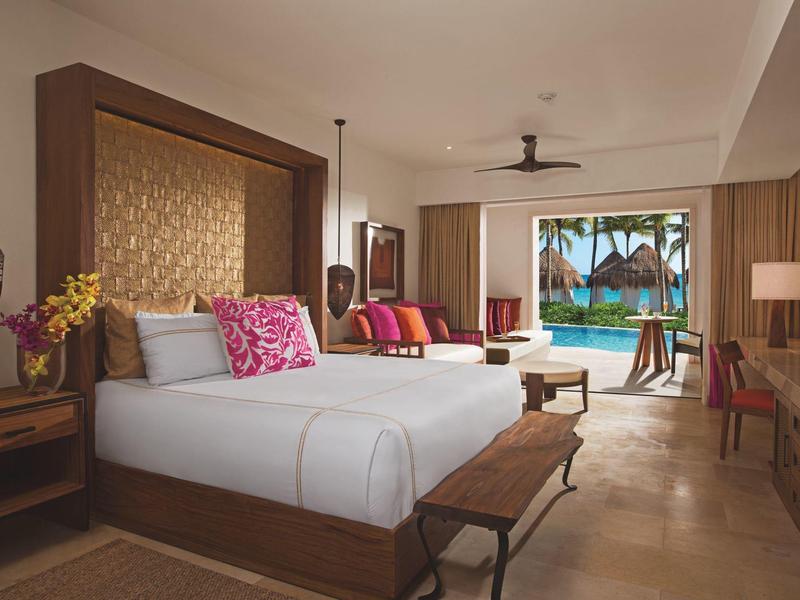 Camera d'hotel di lusso con letto grande, area salotto e vista su piscina e palme.