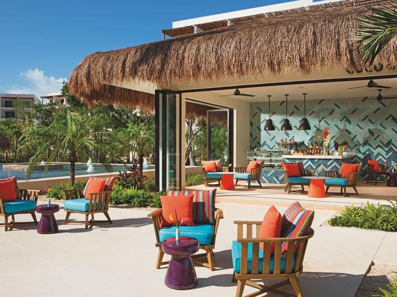 Area lounge aperta e moderna con mobili colorati che si affacciano su piscina e palme.