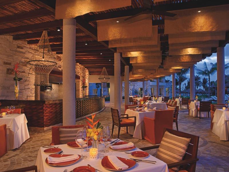 Ristorante elegante con tavoli apparecchiati e soffitto con travi in legno, vista su piscina.
