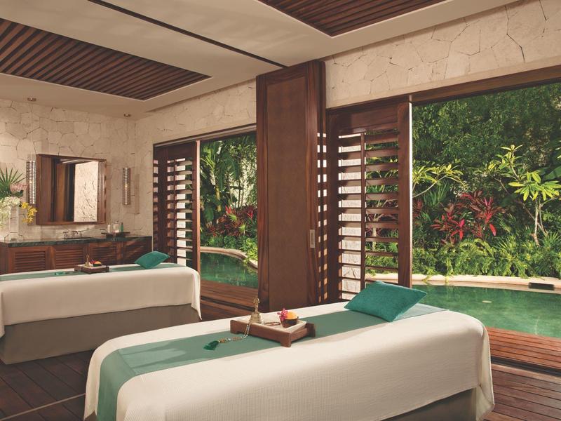 Stanza spa luminosa con due lettini da massaggio con vista su giardino e piscina.