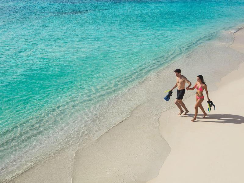 Coppia che cammina su spiaggia di sabbia bianca circondata da acqua turchese limpida.