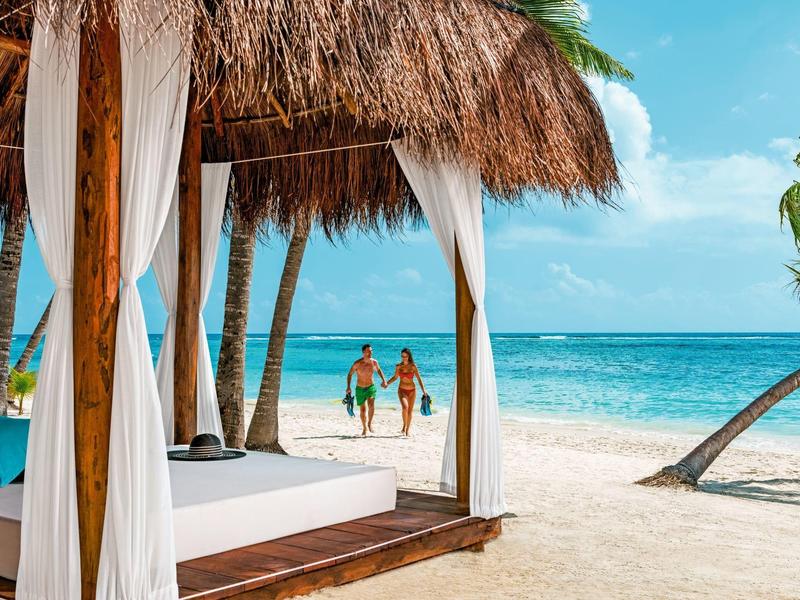 Alloggio romantico con baldacchino sulla spiaggia, coppia che cammina vicino al mare sotto cielo soleggiato