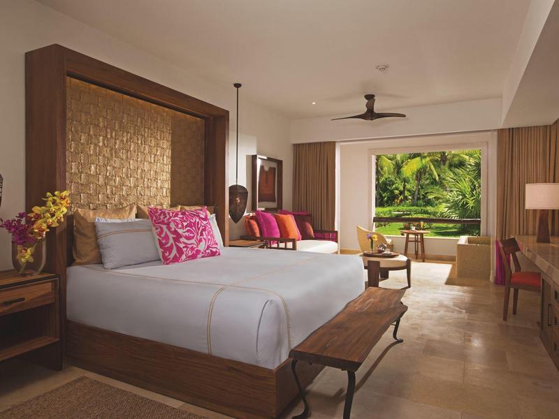 Camera d'hotel luminosa con letto grande, zona salotto e vista aperta sul giardino tropicale.