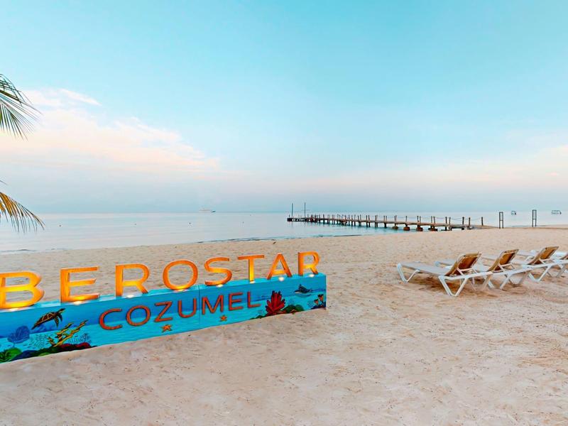 Spiaggia con sdraio e insegna IBEROSTAR COZUMEL vicino al mare calmo all'alba.