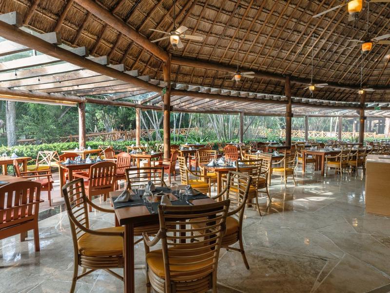 Ristorante all'aperto con mobili in legno e tetto di vetro in ambiente tropicale.