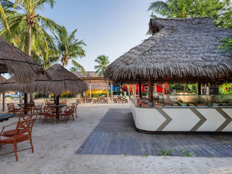 Bar sulla spiaggia con tetto in paglia e posti a sedere sotto palme in una giornata limpida.