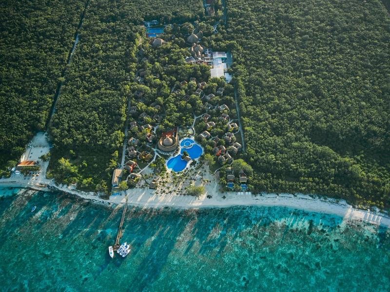 Veduta aerea di una località balneare con più piscine blu e un molo circondati dal verde.