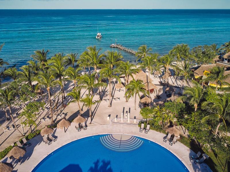 Vista di una piscina d'hotel tropicale con palme e mare sullo sfondo in una giornata soleggiata