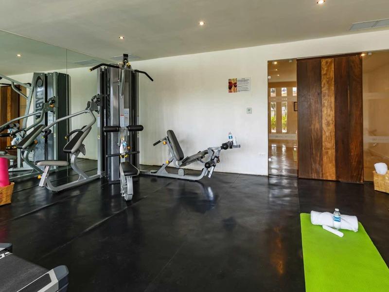 Palestra moderna con vari attrezzi per allenamento e un tappetino yoga verde.