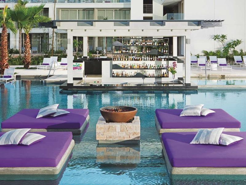 Piscina con lettini viola e bar a bordo piscina in un hotel moderno.