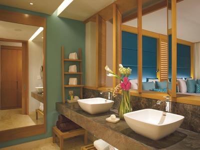 Bagno moderno con doppi lavandini, dettagli in legno, pareti verdi e vaso decorativo con fiori.