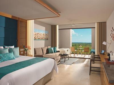 Camera d'hotel moderna con letto grande, zona salotto e balcone con vista panoramica.