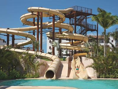 Scivoli d'acqua curvi che sfociano in una piscina circondata da piante tropicali e palme.