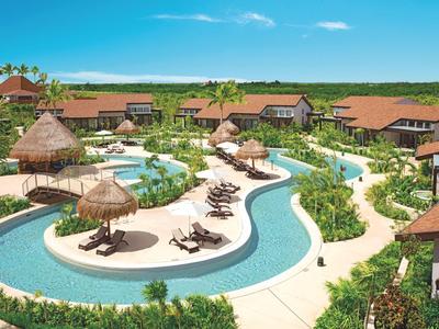 Resort con piscina serpenteante, sombrillas de paja y bungalows circundantes en un entorno tropical