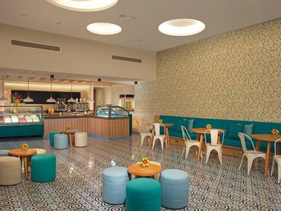 Luminoso ingresso hotel moderno con pavimento a motivi, sedute colorate e banco reception.