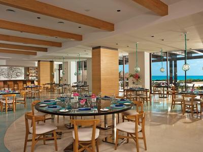 Ampio ristorante dell'hotel con sedie in legno, tavoli rotondi e grandi finestre con vista sul mare.